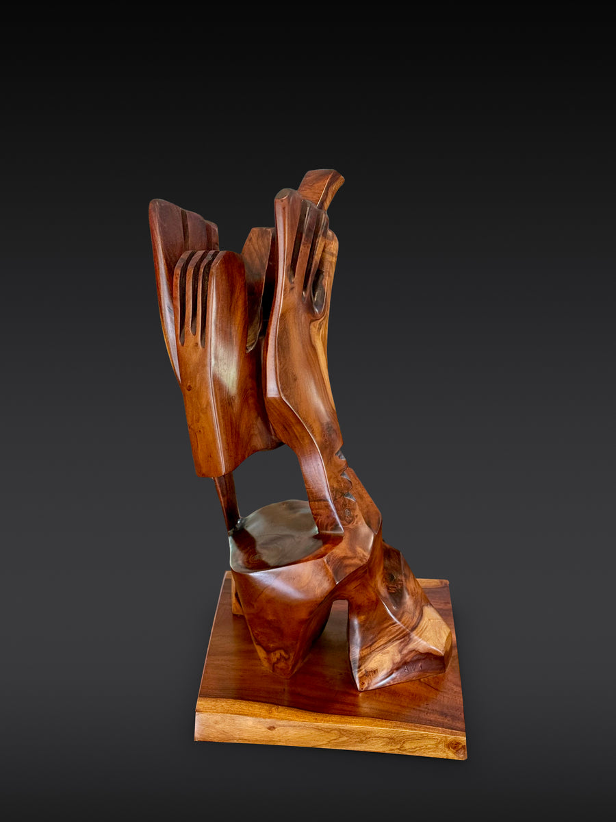 Makaʻāinana | The Commoner, Milo wood sculpture by Avi Molinas: two carved hands holding a head on a square wood plinth, on a dark gray studio backdrop