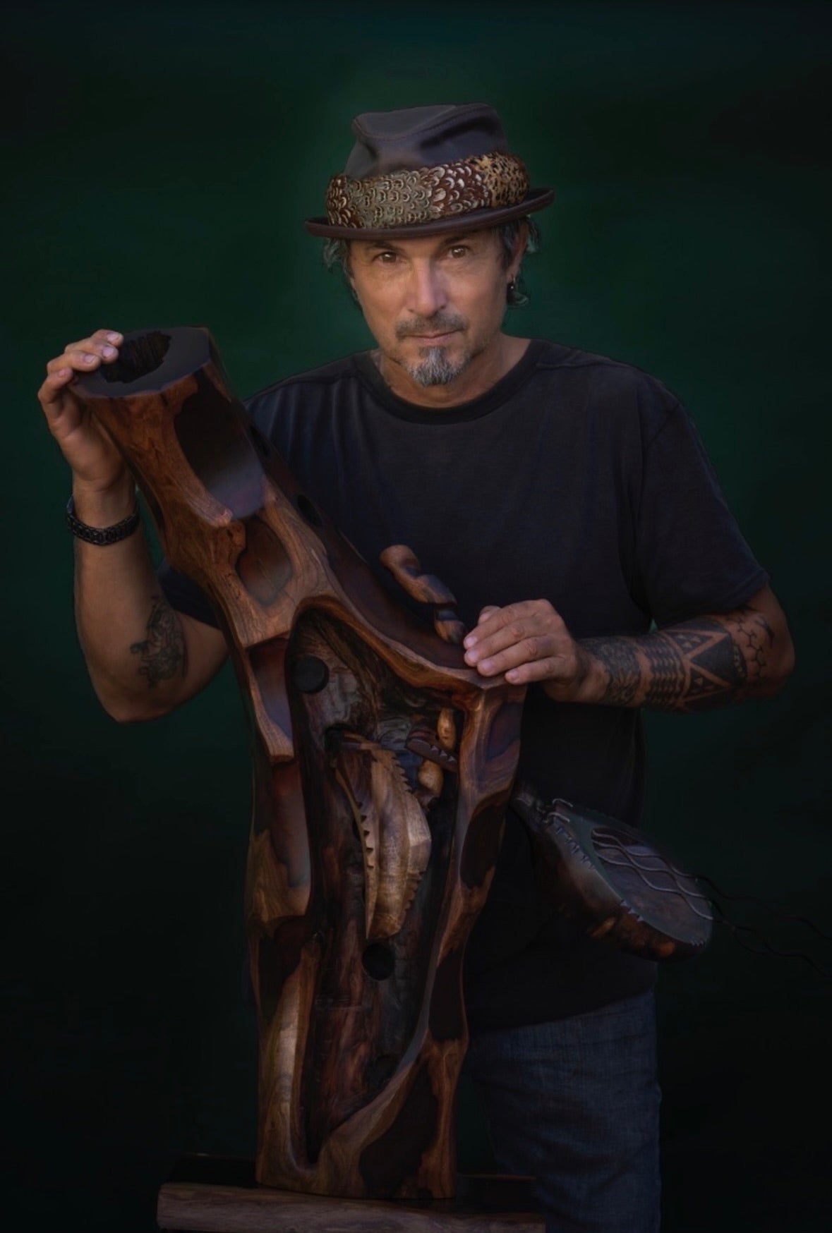 Avi Molinas holding one of his carved wood sculptures against a dark studio background