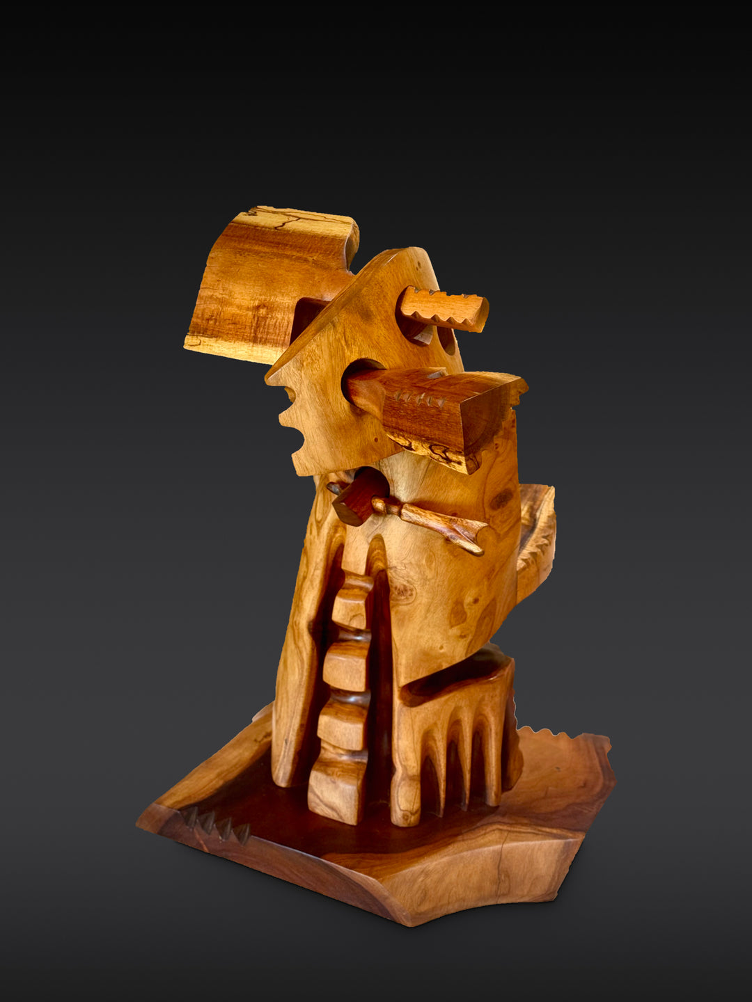Holomua, Milo and Koa wood sculpture by Avi Molinas: a carved figure carrying a piece of Koa, on a wood base, against a dark gray studio backdrop