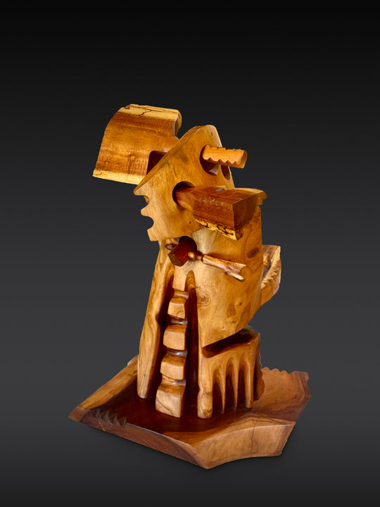 Holomua, Milo and Koa wood sculpture by Avi Molinas: a carved figure carrying a piece of Koa, on a wood base, against a dark gray studio backdrop