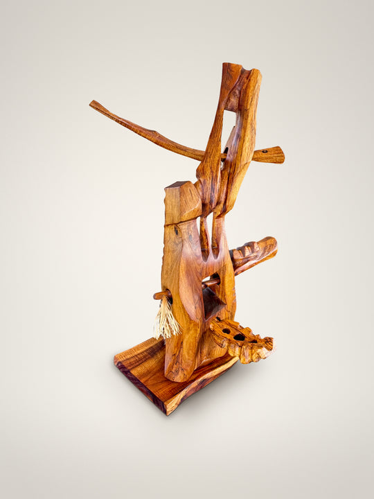 Pono, carved koa wood sculpture by Avi Molinas: an upright form with a long crossing arm and a fiber tassel, on a wood plinth, on a white studio background