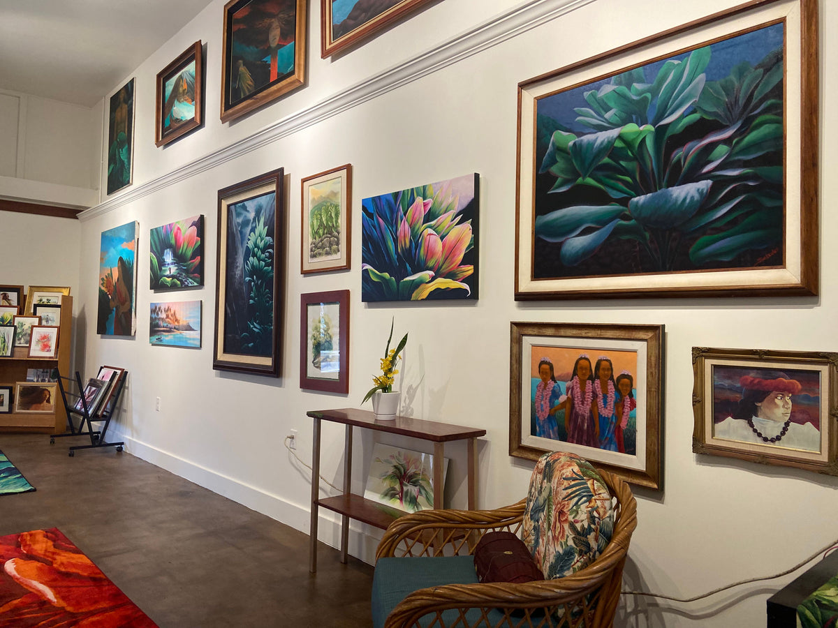 Wailuku-style salon gallery — rattan chair, picture-rail hang, print racks